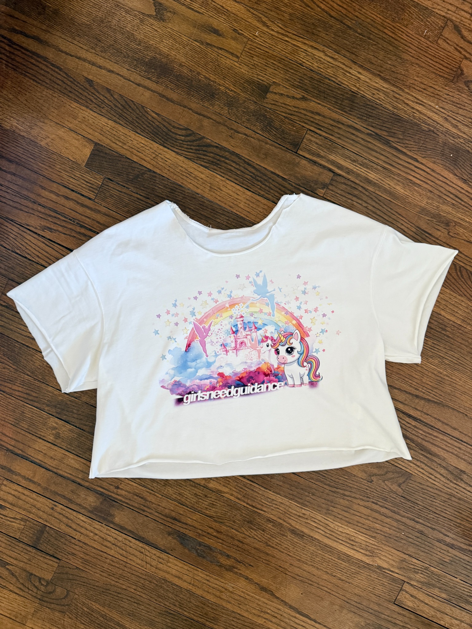 White unicorn castle crop tee on wood floor.