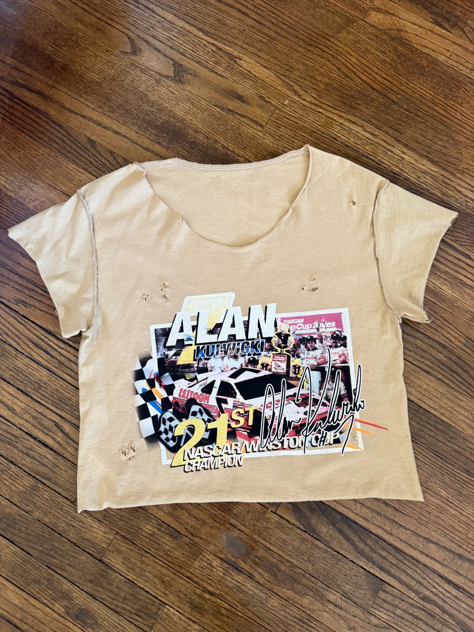 Beige Alan Kulwicki champion crop tee on wood floor.