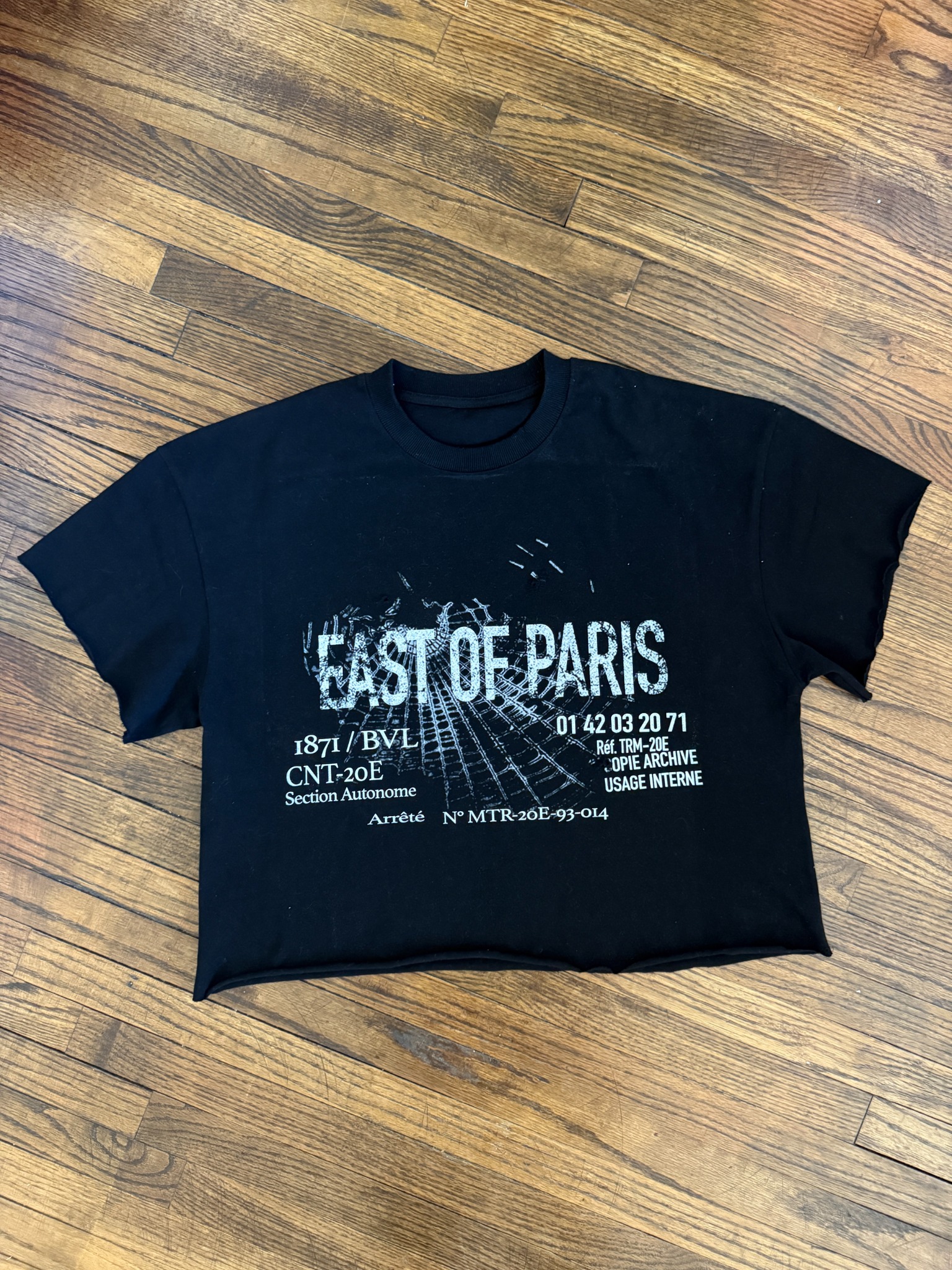 Black East of Paris crop tee on wood floor.